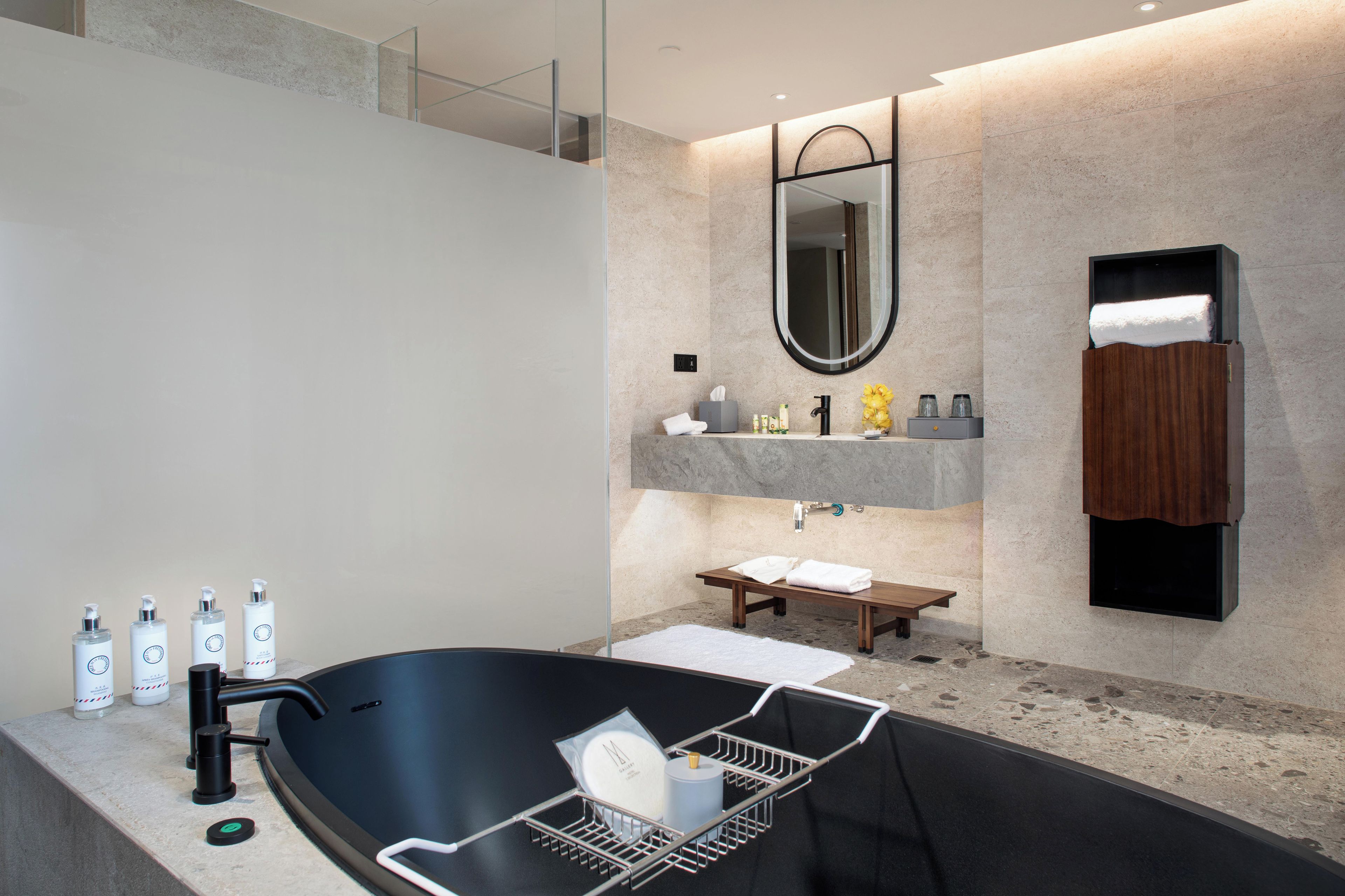 A modern bathroom with a freestanding bathtub, a vanity with a mirror, and a wooden bench.