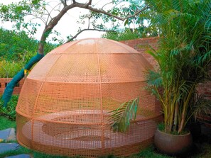 A round, woven structure with a mesh roof, surrounded by greenery and a brick wall. - Dongfengyun Hotel Mi'le-mgallery Collection (Honghe)