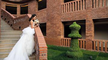 Un vestido de novia en una escalera, un edificio de ladrillo y una escultura topiaria.
