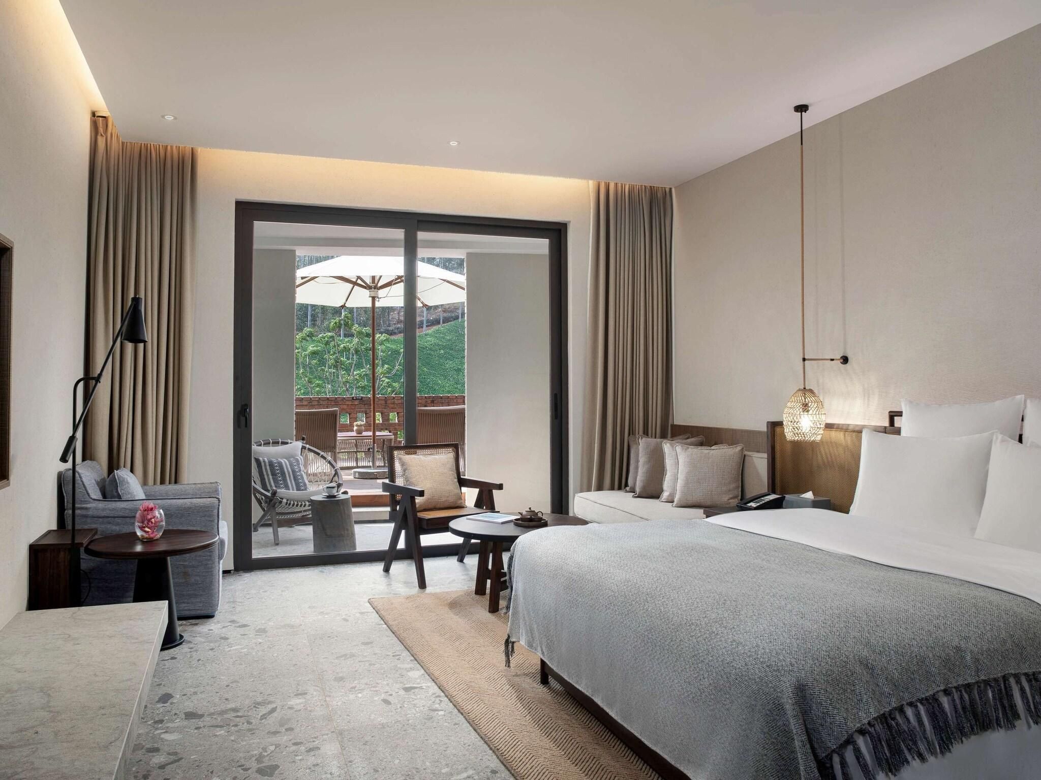 Une chambre d’hôtel avec un lit, un bureau, une chaise, une table et une vue sur la verdure.
