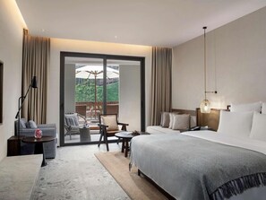 Une chambre d’hôtel avec un lit, un bureau, une chaise, une table et une vue sur la verdure.