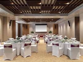 Un salón de conferencias con mesas y sillas blancas, y una pantalla grande.
