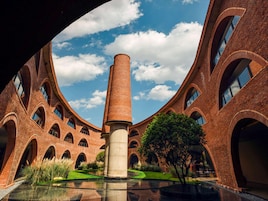 Un edificio con una torre central, ventanas en arco y un patio con un árbol y una fuente de agua.