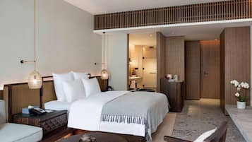 A modern hotel room with a large bed, a sitting area with a coffee table, a small table with a teapot, and a mirror reflecting the bathroom.