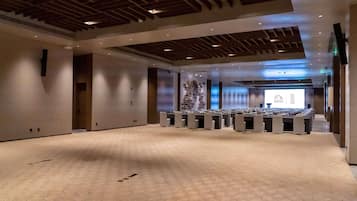 Un amplio salón de conferencias con alfombra estampada, vigas de madera en el techo y una pantalla de proyección al frente.