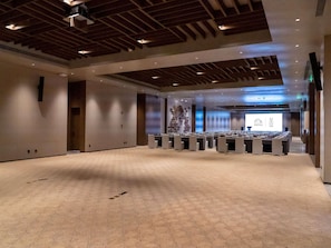 Un amplio salón de conferencias con alfombra estampada, vigas de madera en el techo y una pantalla de proyección al frente.