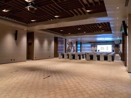 Un amplio salón de conferencias con alfombra estampada, vigas de madera en el techo y una pantalla de proyección al frente.