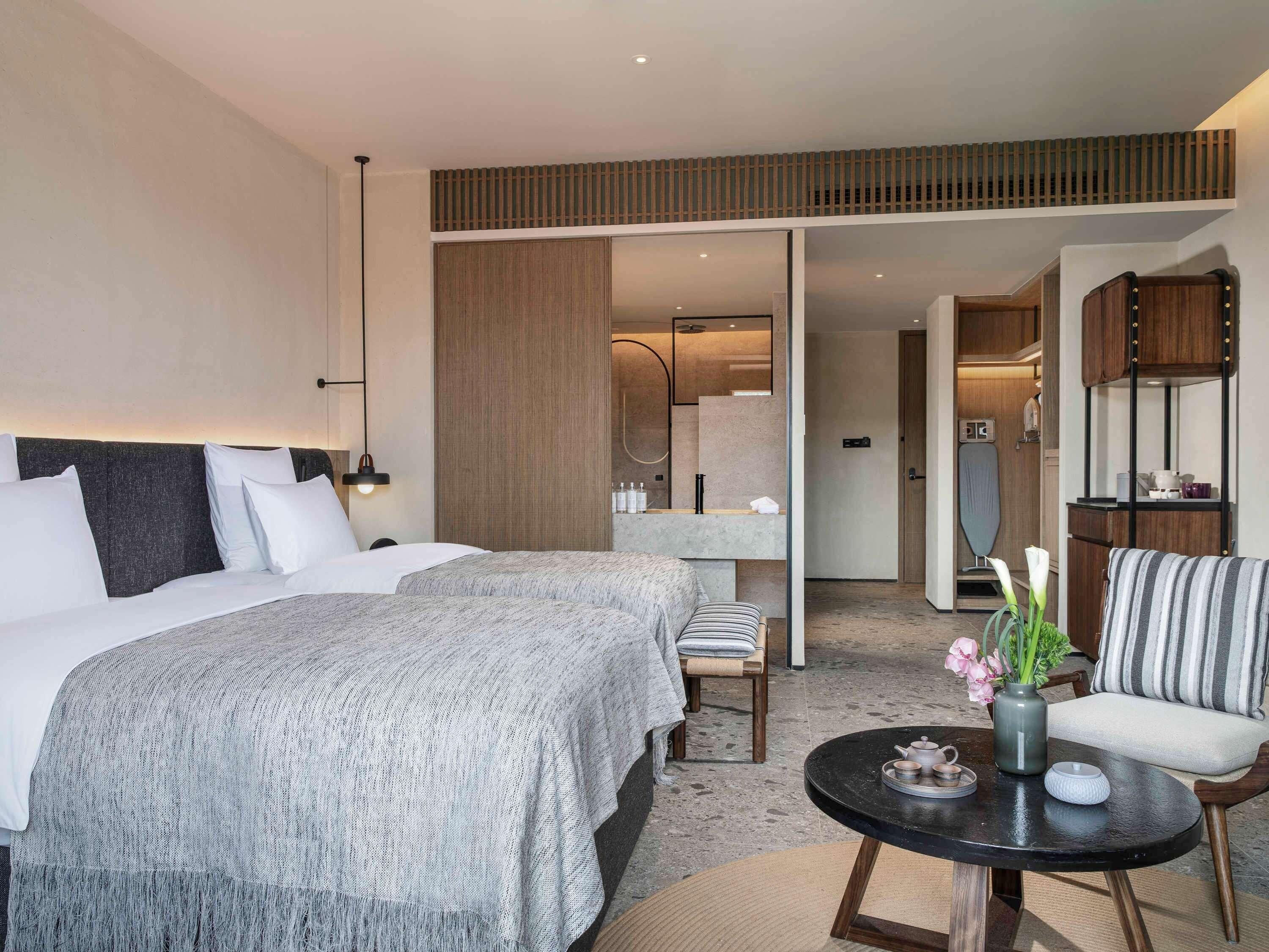 Habitación de hotel con una cama grande, una zona de estar con mesa y un baño visible a través de una puerta abierta.