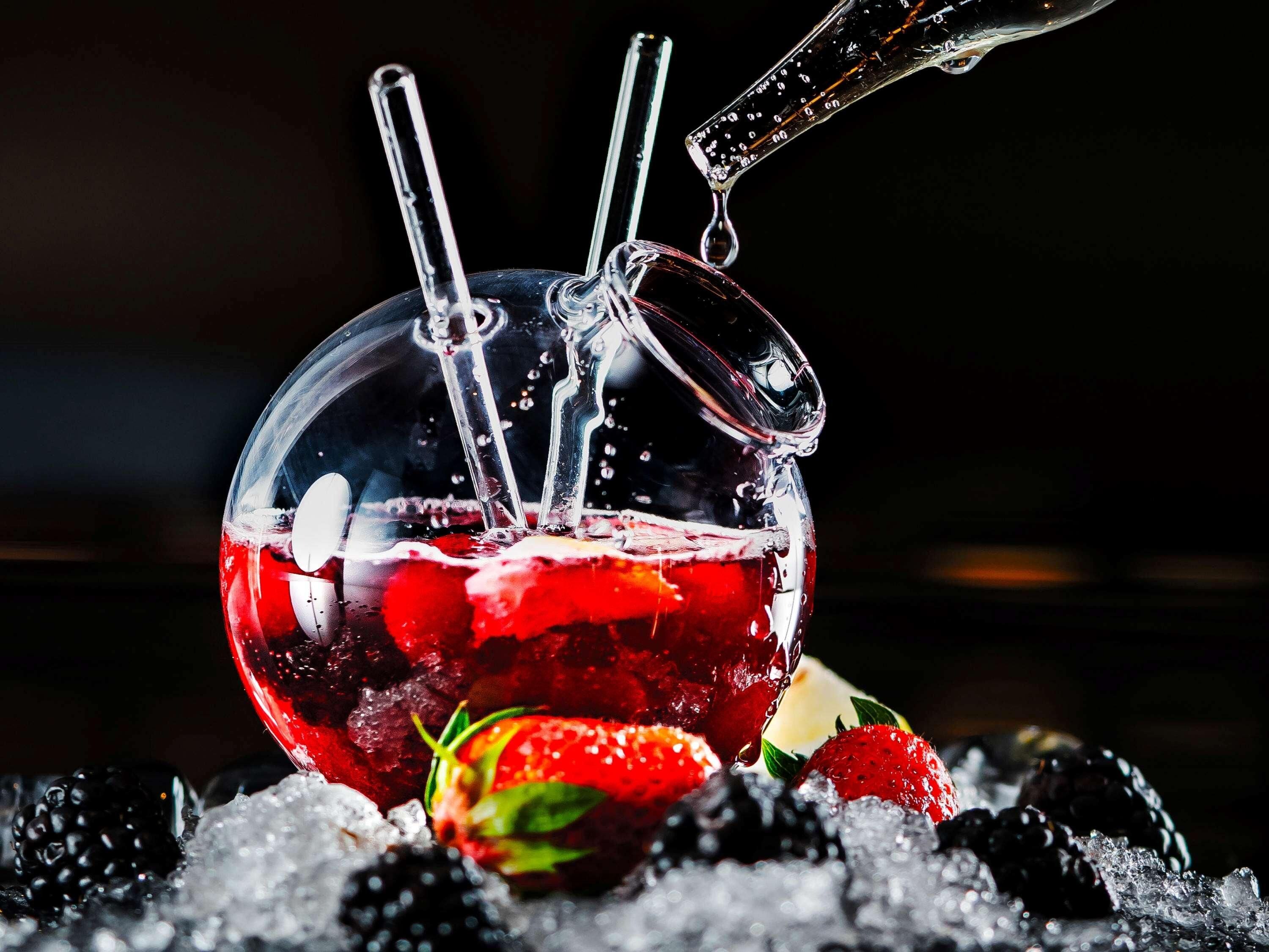 A clear glass with a handle, filled with ice and berries, with water being poured in.