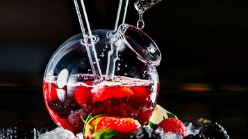 A clear glass with a handle, filled with ice and berries, with water being poured in.