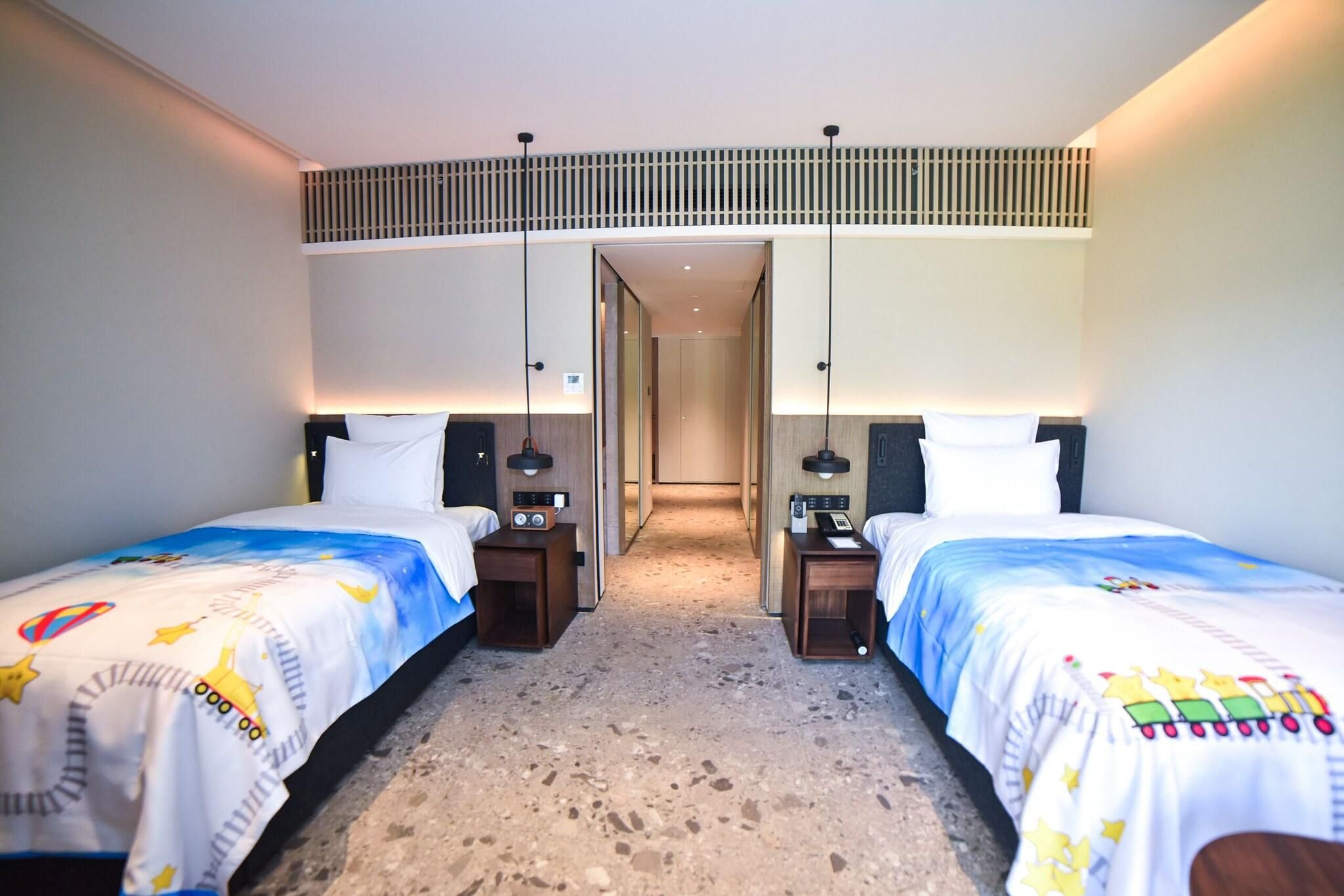 Una habitación de hotel con dos camas, un pasillo y una rejilla de ventilación en el techo.