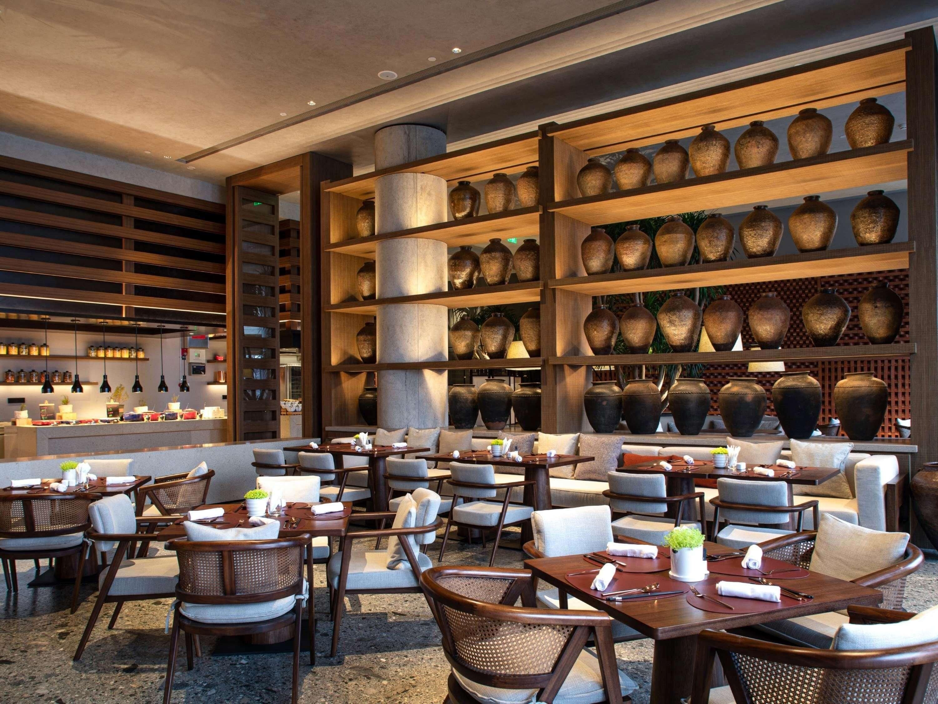 Un restaurante con varias mesas y sillas, una zona de bar y estanterías con jarrones grandes.