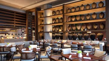 Un restaurante con varias mesas y sillas, una zona de bar y estanterías con jarrones grandes.