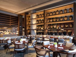 Un restaurante con varias mesas y sillas, una zona de bar y estanterías con jarrones grandes.