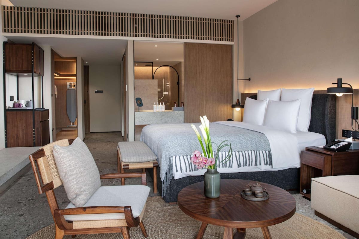 A hotel room with a bed, a desk, a chair, a round table, and a bathroom visible through an open door.