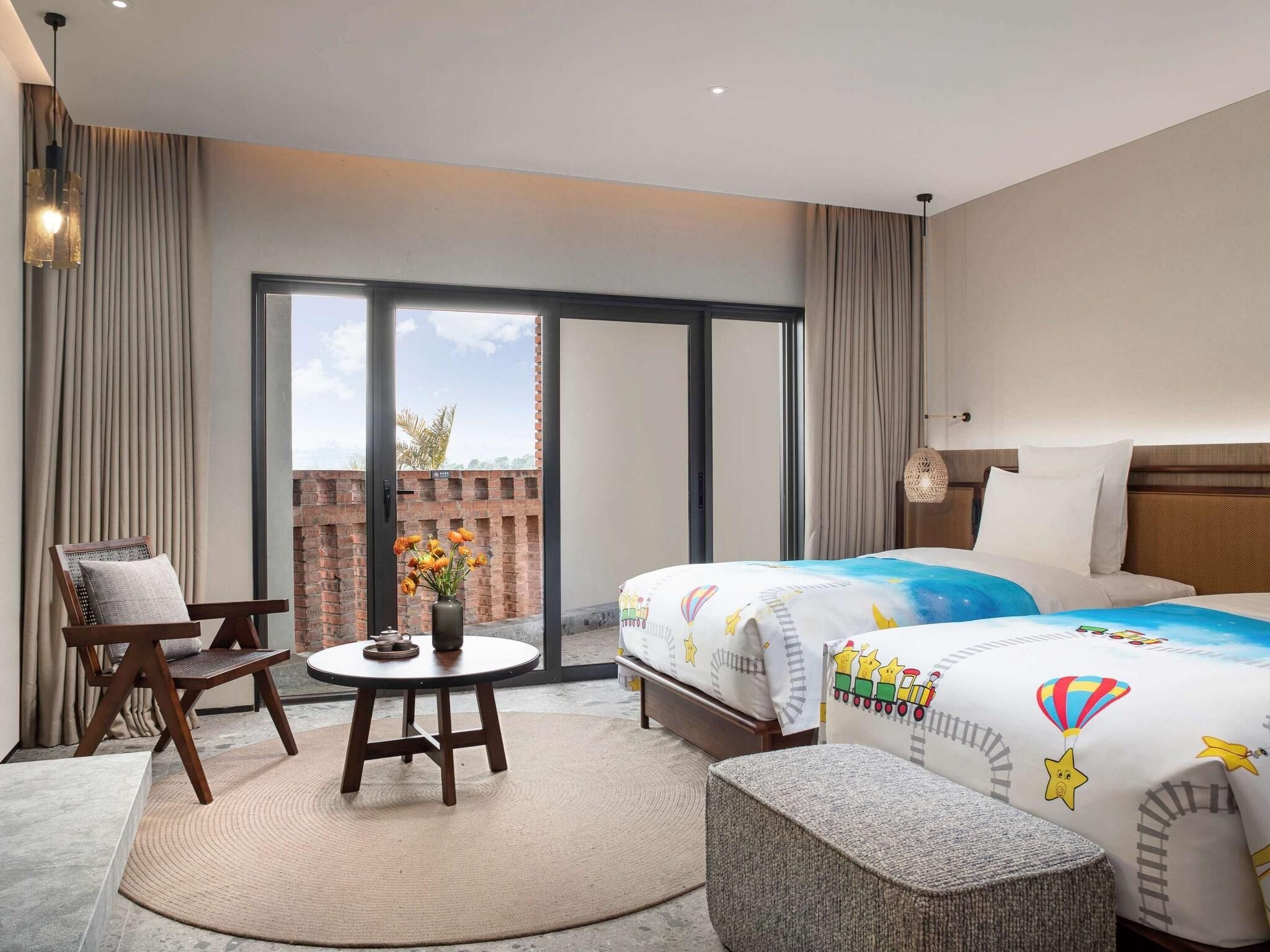 Habitación de hotel con cama, una silla, una mesita y vistas al exterior.