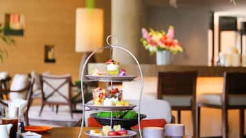 A three-tiered dessert stand with various sweets and a cup of tea on a table in a hotel room.