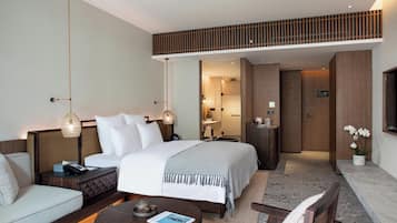 Habitación de hotel con cama, mesitas de noche, sofá, mesa de centro y baño visible a través de una puerta abierta.
