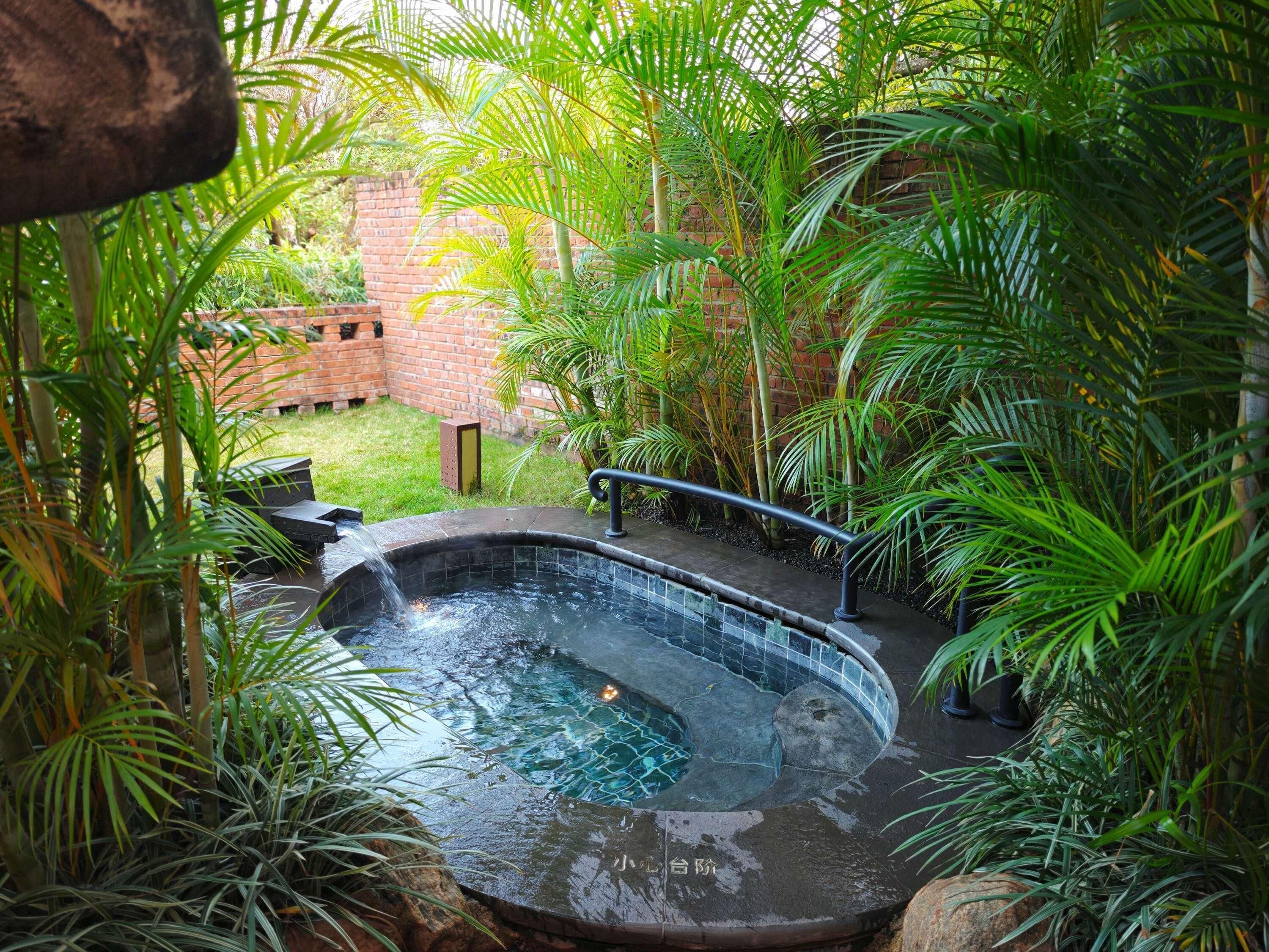 Un jacuzzi rodeado de exuberante follaje y un muro de ladrillo.