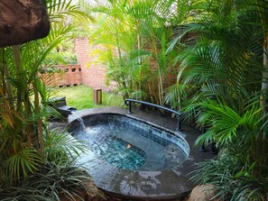 Un jacuzzi rodeado de exuberante follaje y un muro de ladrillo.