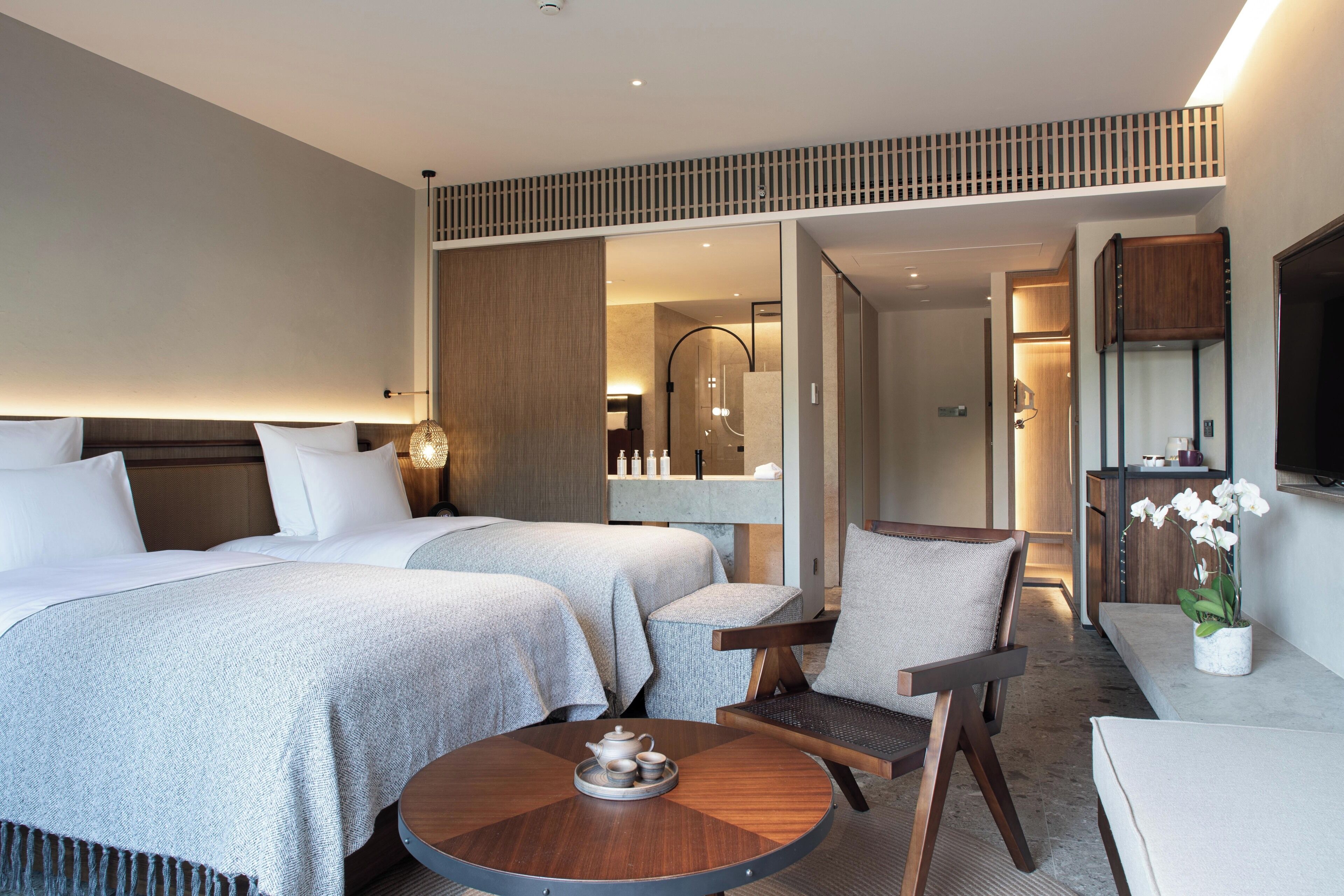 Habitación de hotel con dos camas, una zona de estar con una mesa redonda, un televisor y un baño visible a través de una puerta abierta.