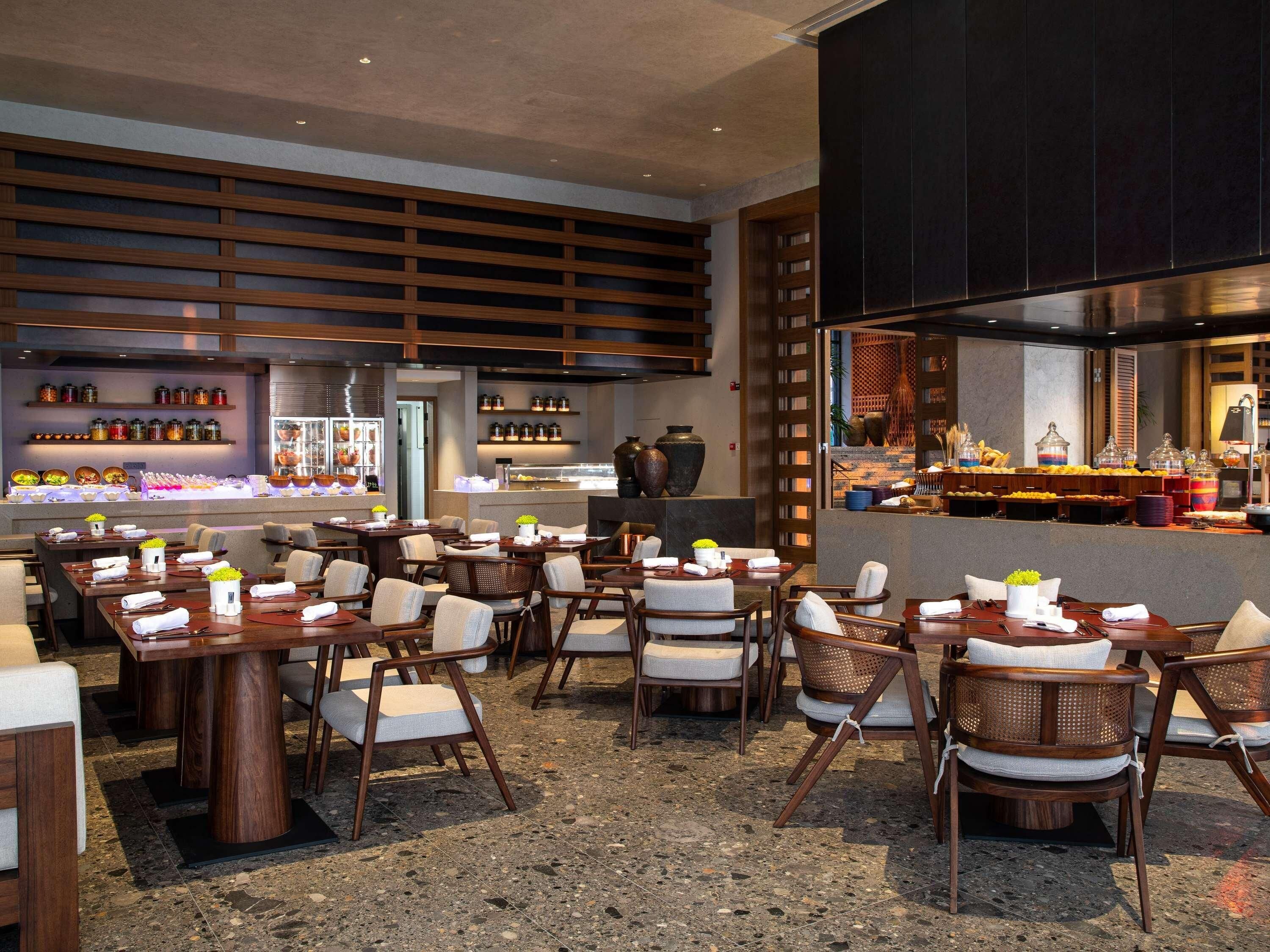 A restaurant with multiple dining tables and chairs, a kitchen area, and shelves with jars and decorative items.
