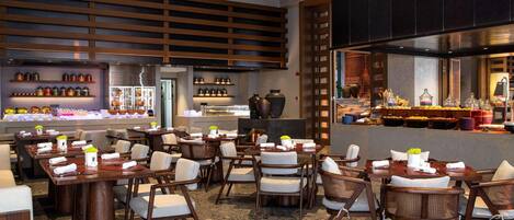 Un restaurante con varias mesas y sillas, una zona de cocina y estantes con frascos y objetos decorativos.