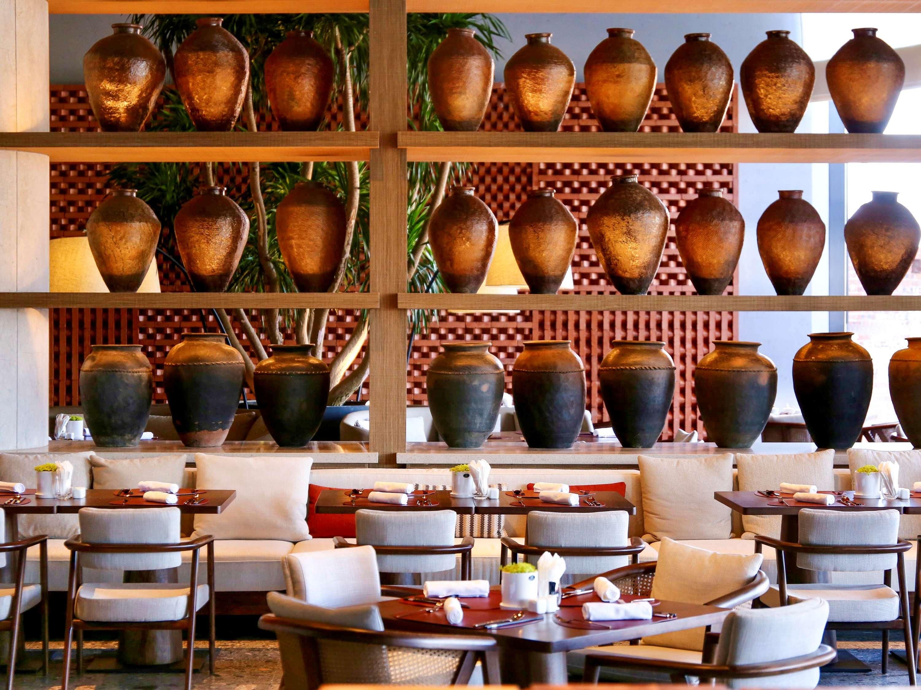 Un restaurante con varias mesas y sillas, una variedad de jarrones en estanterías y un papel tapiz con diseño en el fondo.