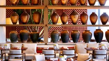 A restaurant with multiple tables and chairs, a variety of vases on shelves, and a patterned wall in the background.