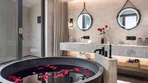 Un baño moderno con una bañera grande, dos espejos montados en la pared, una encimera de mármol y un florero con flores rojas.