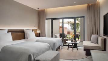A hotel room with two beds, a sofa, a TV, and a balcony with outdoor furniture.