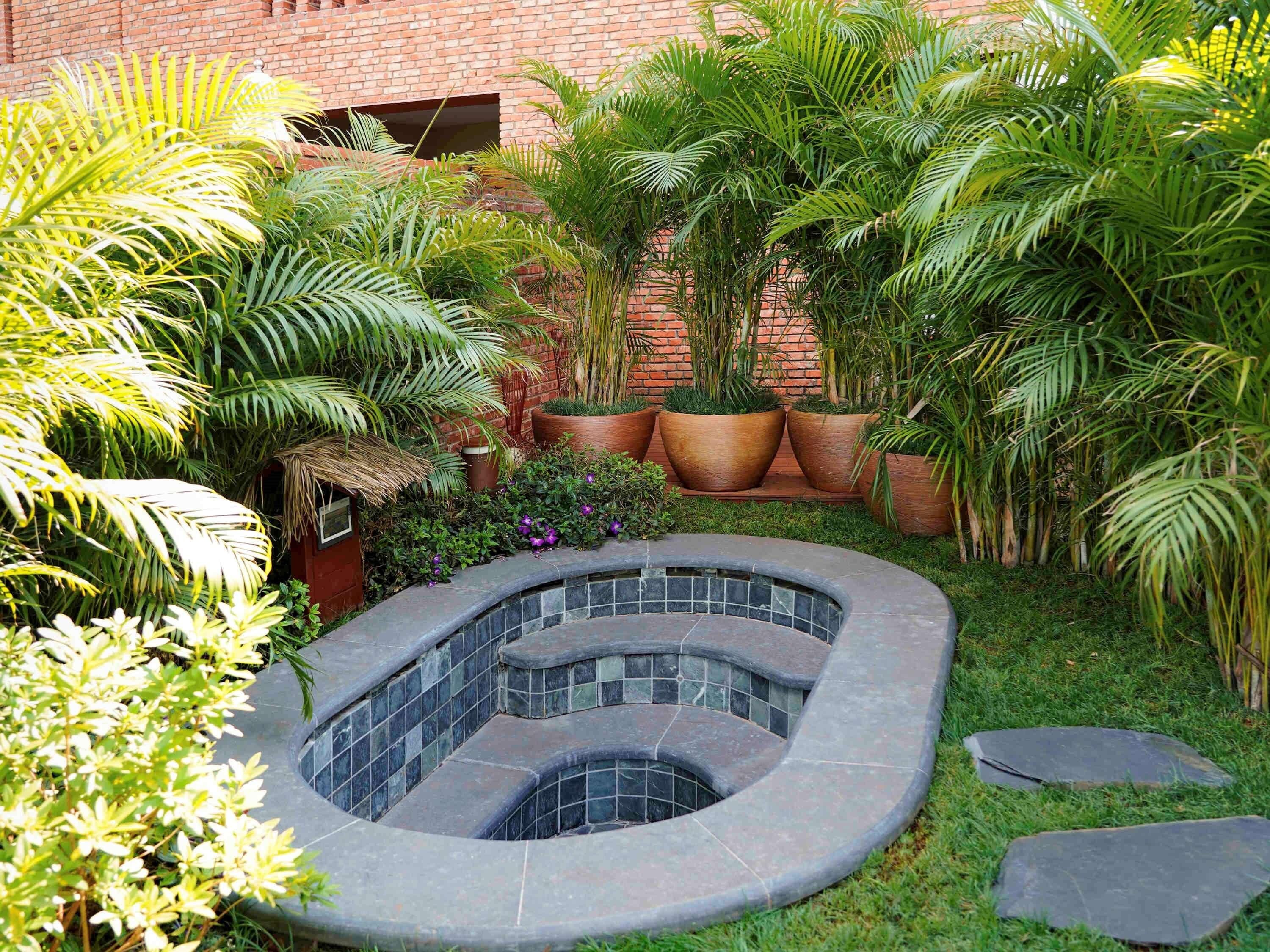 Un jardín con jacuzzi, plantas en macetas y un muro de ladrillo.