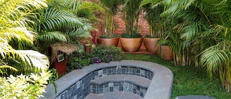 Un jardín con jacuzzi, plantas en macetas y un muro de ladrillo.