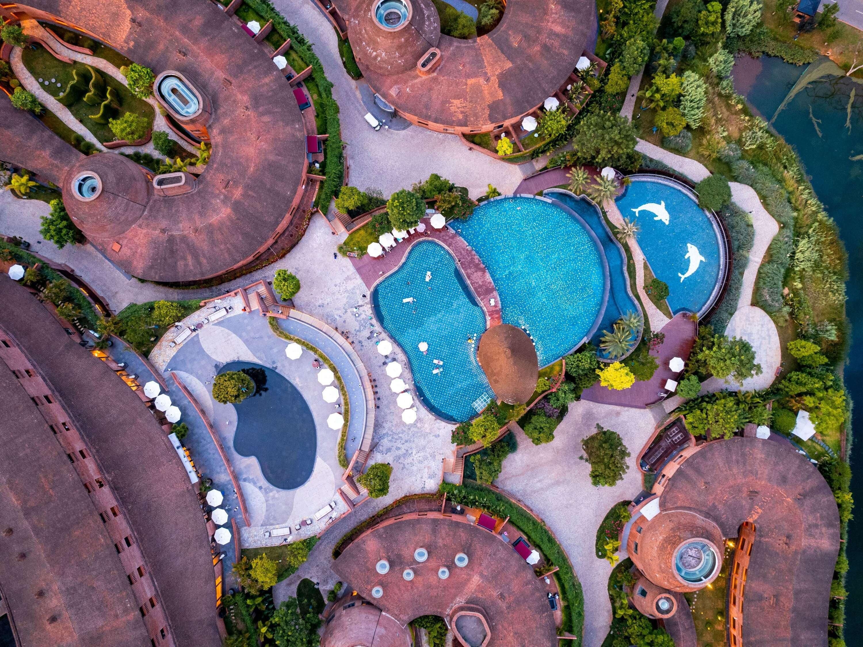 An aerial view of a resort with multiple swimming pools, circular structures, and surrounding greenery.