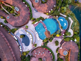 An aerial view of a resort with multiple swimming pools, circular structures, and surrounding greenery.