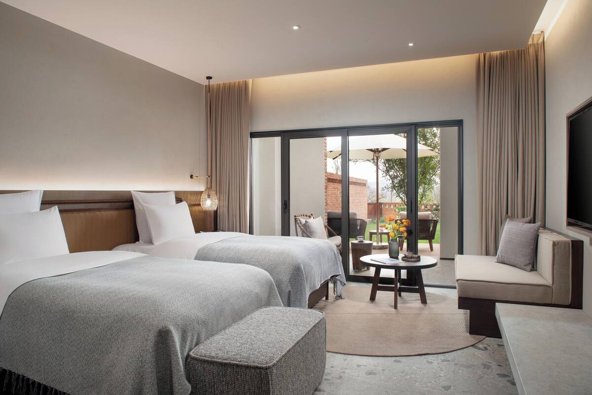 A hotel room with two beds, a sofa, a TV, and a balcony with outdoor furniture.