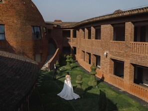 A courtyard with a brick building, a staircase, and a bride in a white dress.