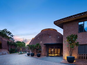A building with a curved brick facade, a glass entrance, and potted plants. - Dongfengyun Hotel Mi'le-mgallery Collection (Honghe)