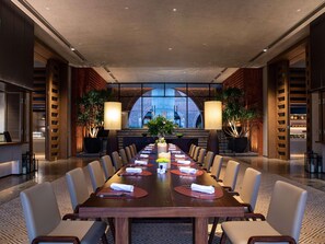 Un salón de conferencias con una larga mesa, sillas y plantas en macetas.