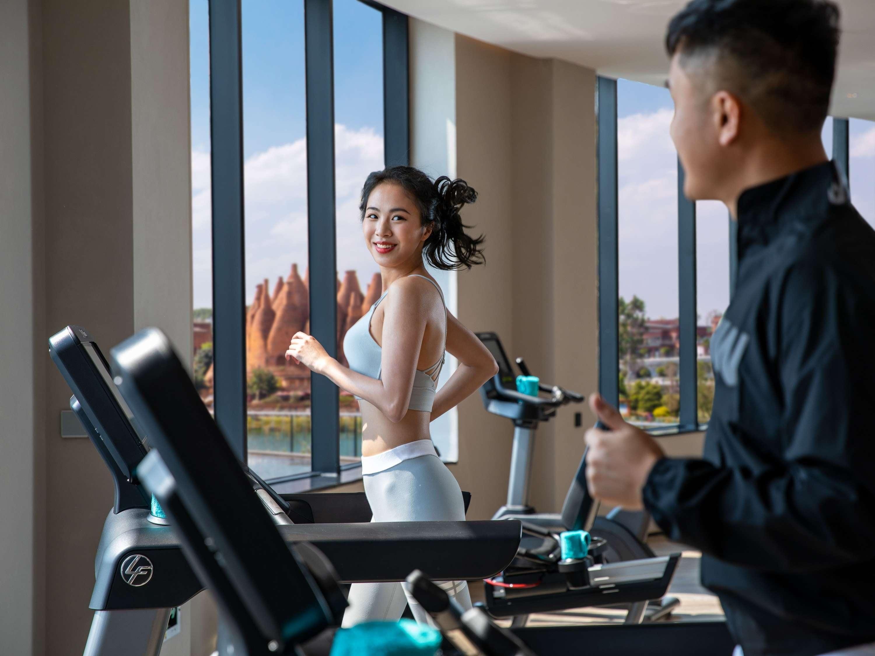 A gym with treadmills, a person exercising, and a large window with a view of rock formations.