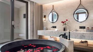 Un baño moderno con una bañera grande, dos espejos redondos, una encimera de mármol y un florero con flores rojas.