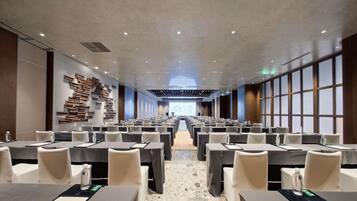 A conference room with rows of tables and chairs, a modern ceiling design, and a large screen at the front.