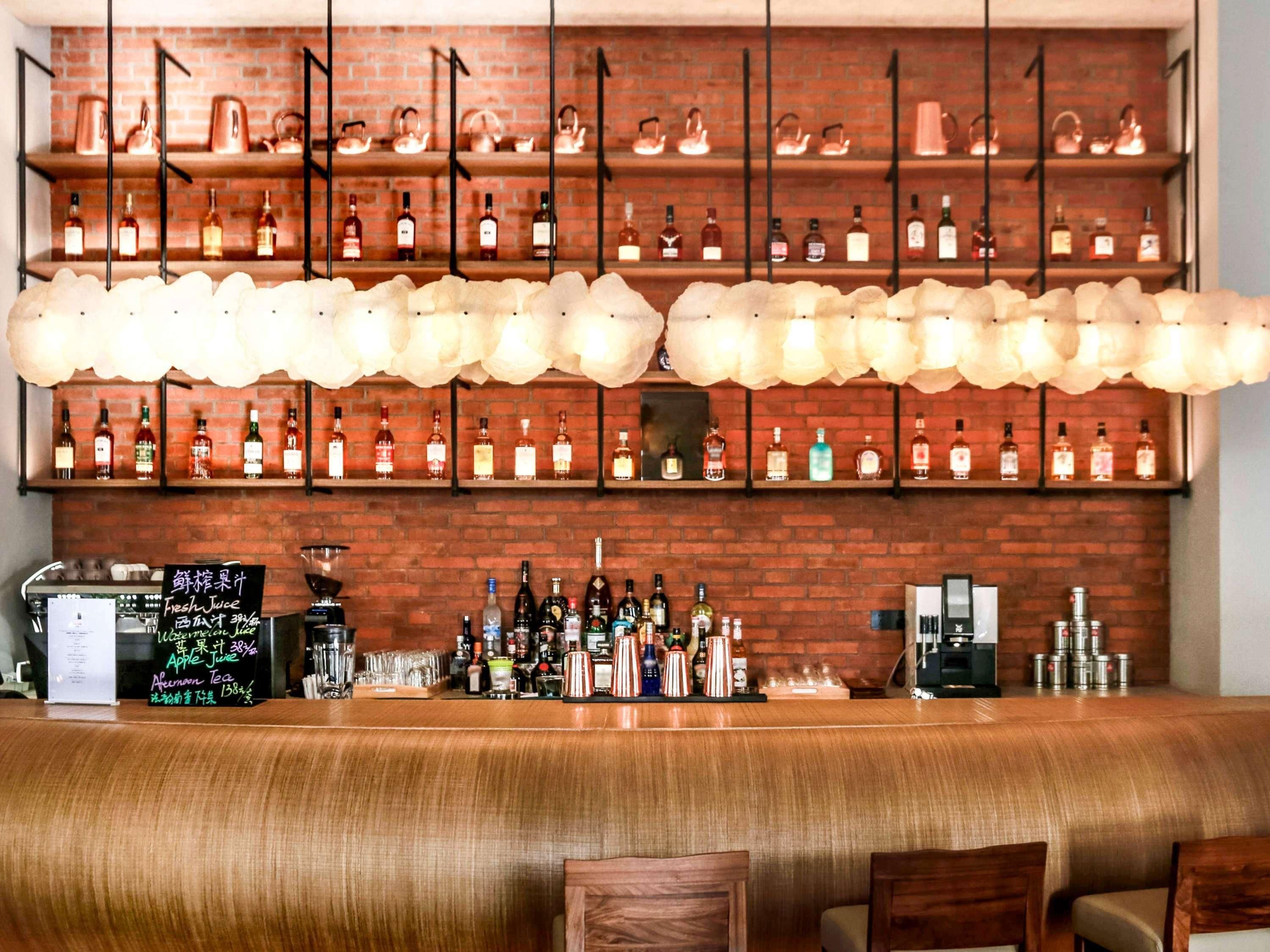 Una zona de bar con estantes de botellas de licores, una máquina de café y un cartel con la carta.
