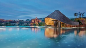 Un resort con piscina, una estructura de techo de paja y montañas al fondo.
