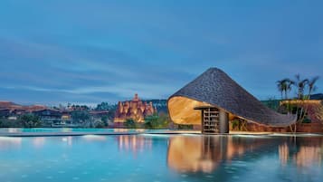 Un resort con piscina, una estructura de techo de paja y montañas al fondo.