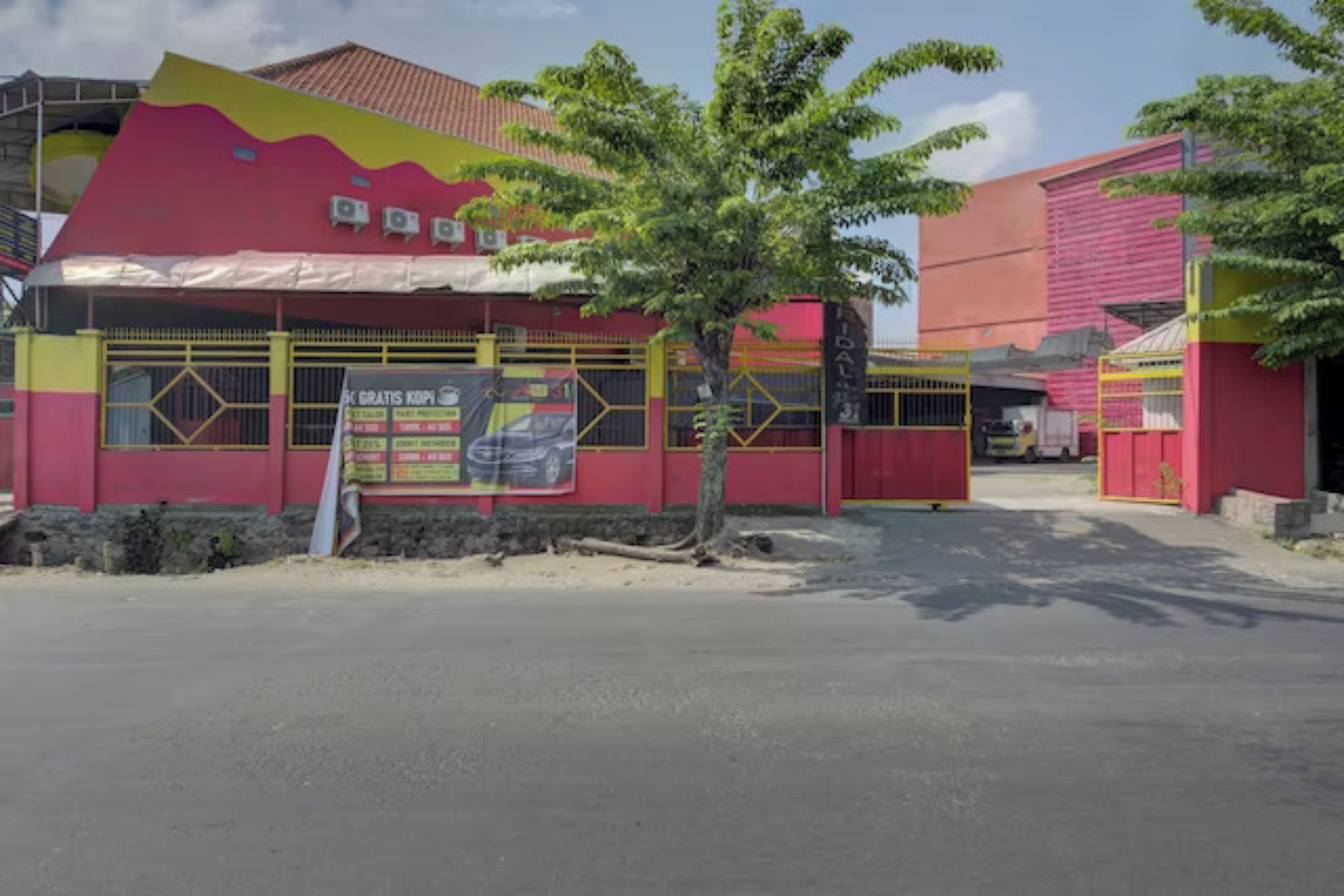 A building with a red and yellow facade, a tree in front, and a signboard.