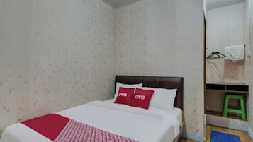 A bedroom with a bed, a red and white patterned bedspread, two red pillows, a wooden headboard, a green stool, and a blue mat on the floor.