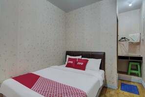 A bedroom with a bed, a red and white patterned bedspread, two red pillows, a wooden headboard, a green stool, and a blue mat on the floor. - Super OYO 3198 Sukomanunggal Inn (Surabaya)