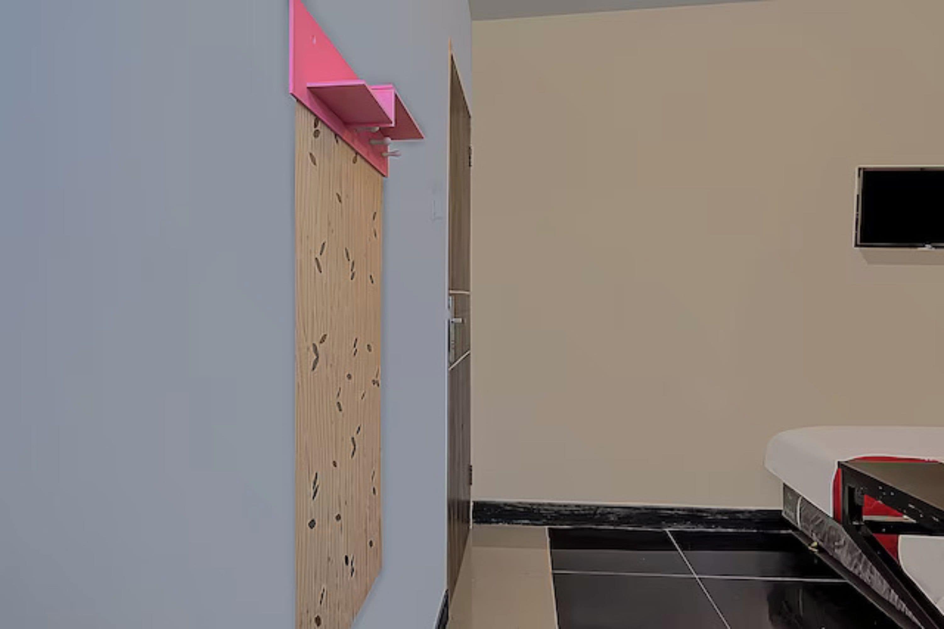 A room with a wooden wardrobe, a television mounted on the wall, and a bed with a red and white headboard.