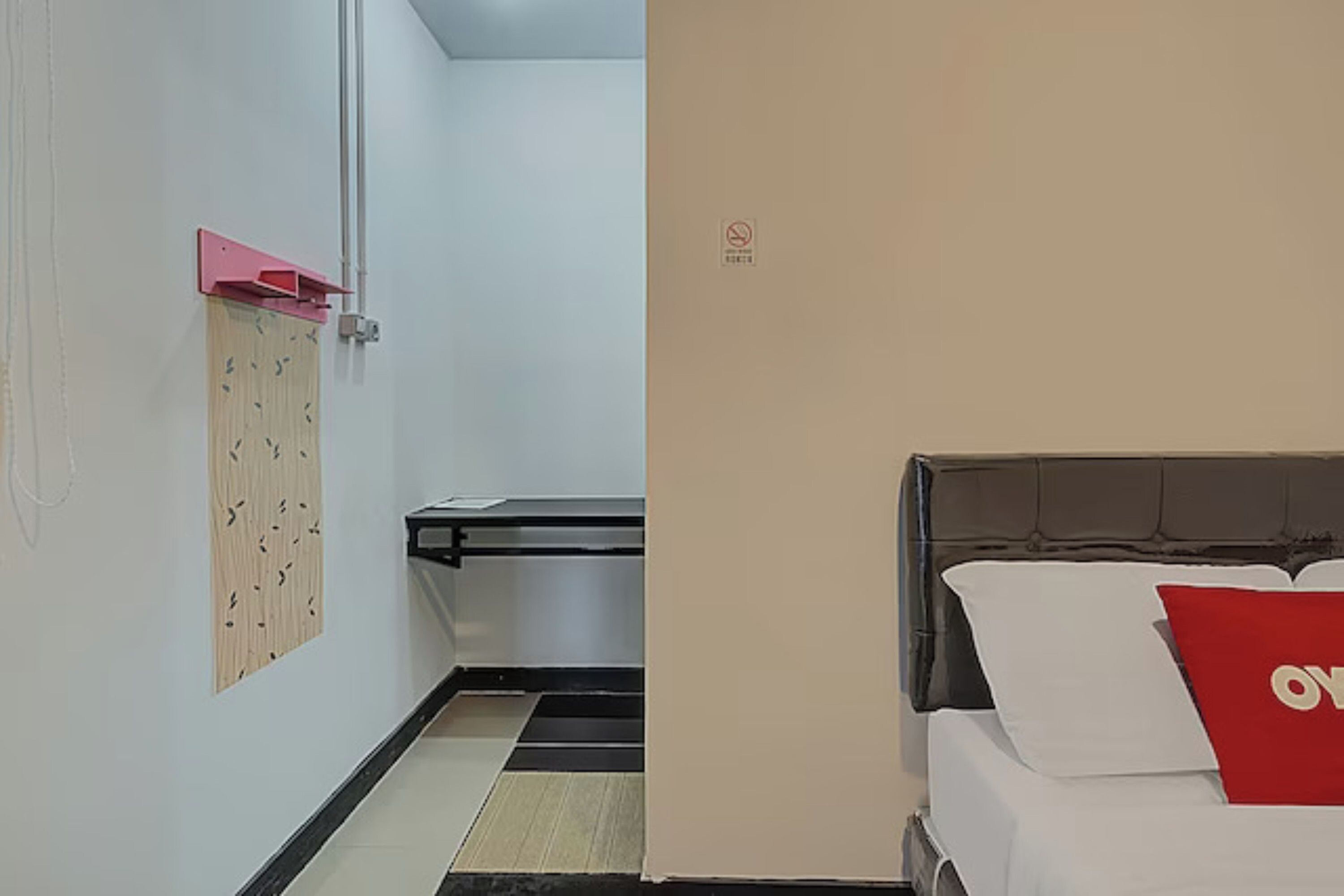 A hotel room with a bed, a red pillow, a wooden panel on the wall, and a trash bin.